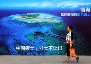 FILE - In this July 14, 2016 file photo, a woman walks past a billboard featuring an image of an island in South China Sea on display with Chinese words that read: "South China Sea, our beautiful motherland, we won't let go an inch" in Weifang in east China's Shandong province. Two state-owned companies have announced plans to develop floating nuclear reactors for use by oil rigs or island communities. If they succeed, the achievement would raise concern the reactors might be sent into harm’s way to support oil exploration in the South China Sea, where Beijing faces conflicting territorial claims by neighbors including Vietnam and the Philippines. (Chinatopix via AP, File) CHINA OUT